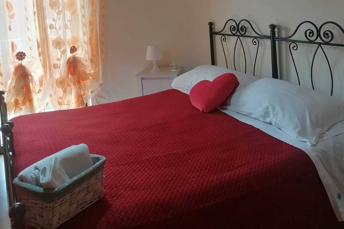Un dormitorio con cama, mesita de noche, lámpara, cesta y un cuadro en la pared.