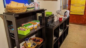 Ein Zimmer mit Essbereich, das ein Gemälde einer Küstenszene, einen Kühlschrank, Regale mit Lebensmitteln und einen Mülleimer zeigt.
