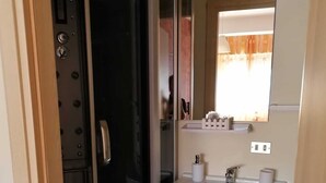 Ein Badezimmer mit Duschabtrennung aus Glas, einem weißen Waschbecken mit Spiegel darüber und einem kleinen Schrank.