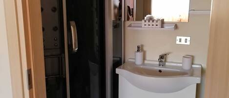 A bathroom with a glass shower door, a white sink with a mirror above it, and a small storage cabinet.