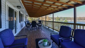 A covered deck with outdoor furniture, a table with a plant, and a view of a lake.