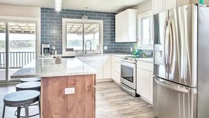 A modern kitchen with a large island, stainless steel appliances, and a view to the outside.