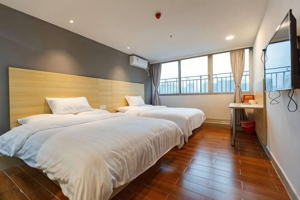 Ein Hotelzimmer mit zwei Betten, einem Fernseher, einem Fenster mit Vorhängen und einem Holzboden.