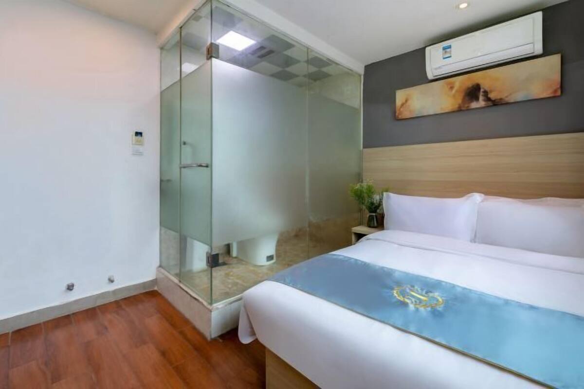Ein Hotelzimmer mit einer gläsernen Duschkabine, einem Bett mit blauer und goldener Bettdecke, einem Holzkopfschild und einem Bild an der Wand.
