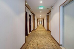Een hotelgang met een kamerbreed tapijt, deuren aan beide zijden en een lamp aan het plafond.