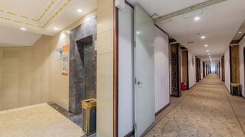 A hotel corridor with a tiled floor, a glass elevator, and a door with a wooden frame.