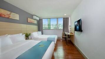 Habitación de hotel con dos camas, un escritorio pequeño, una silla, ventana con vistas y obras de arte en las paredes.