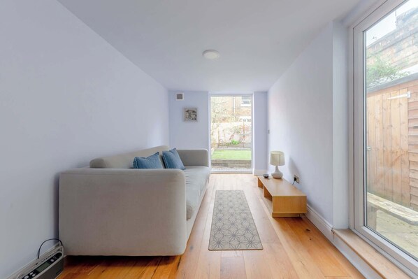 A modern living room with a sofa, a rug, a lamp, and a view of the backyard. - Garden| Full Kitchen| King Bed| Modern bathroom (London)