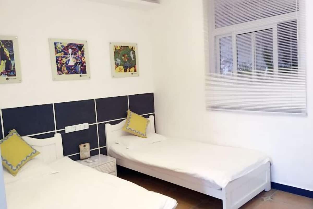 Una habitación con dos camas, una ventana con persianas y tres cuadros enmarcados en la pared.