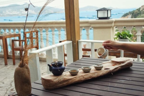 A wooden table with a tray holding a teapot and cups, a vase with dried branches, and a hand pouring tea.