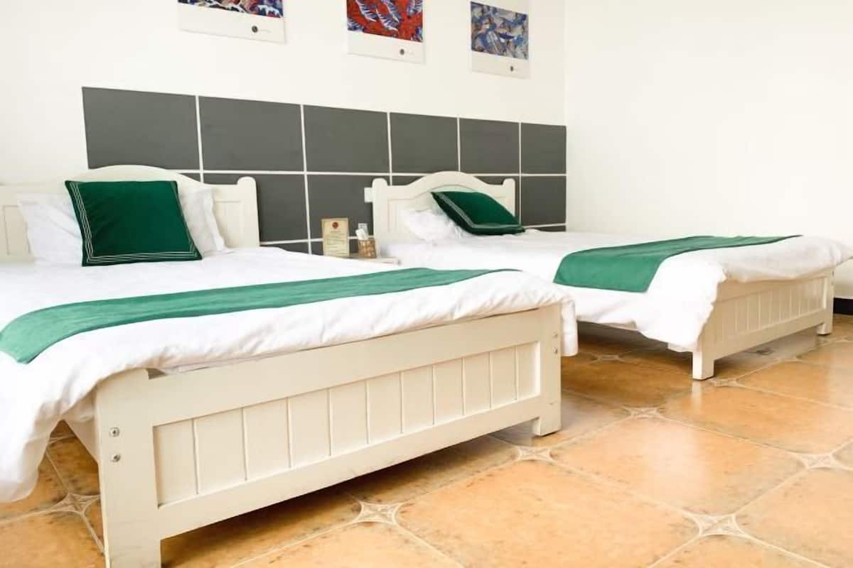 Habitación con dos camas, cada una con cabeceros blancos y ropa de cama verde.