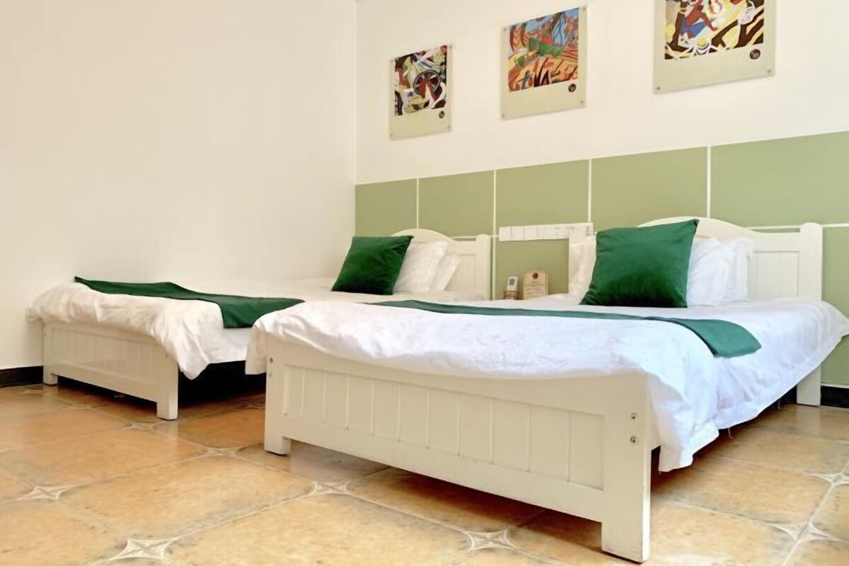 Une chambre avec deux lits simples, chacun doté d’une tête de lit blanche et d’une literie verte. La chambre a un sol carrelé et un mur d’accent de couleur verte.