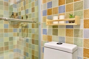 Un baño con cabina de ducha de vidrio, un inodoro y un estante con artículos de aseo.