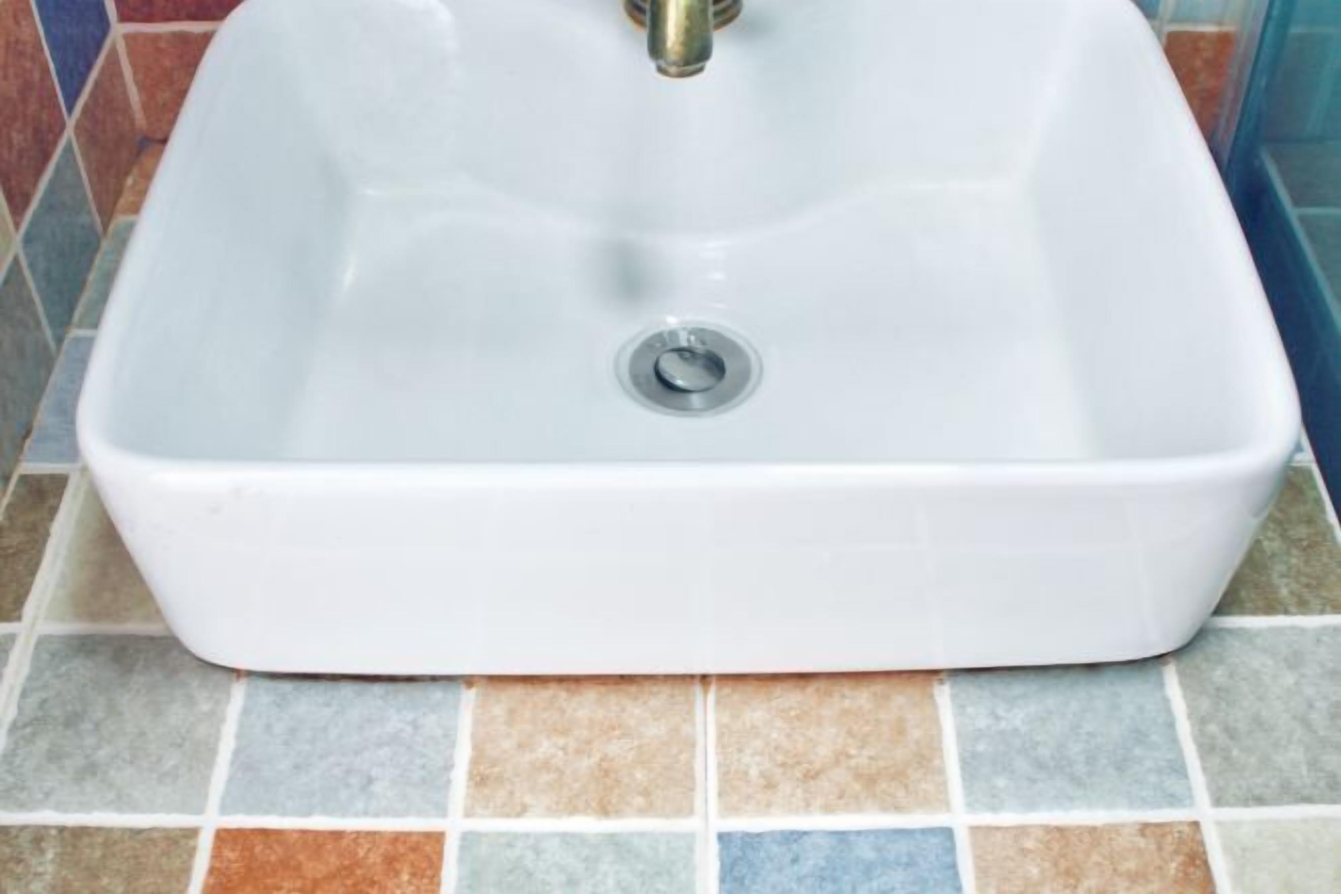 Un lavamanos rectangular blanco con desagüe, sobre un piso de baldosas con un diseño multicolor.