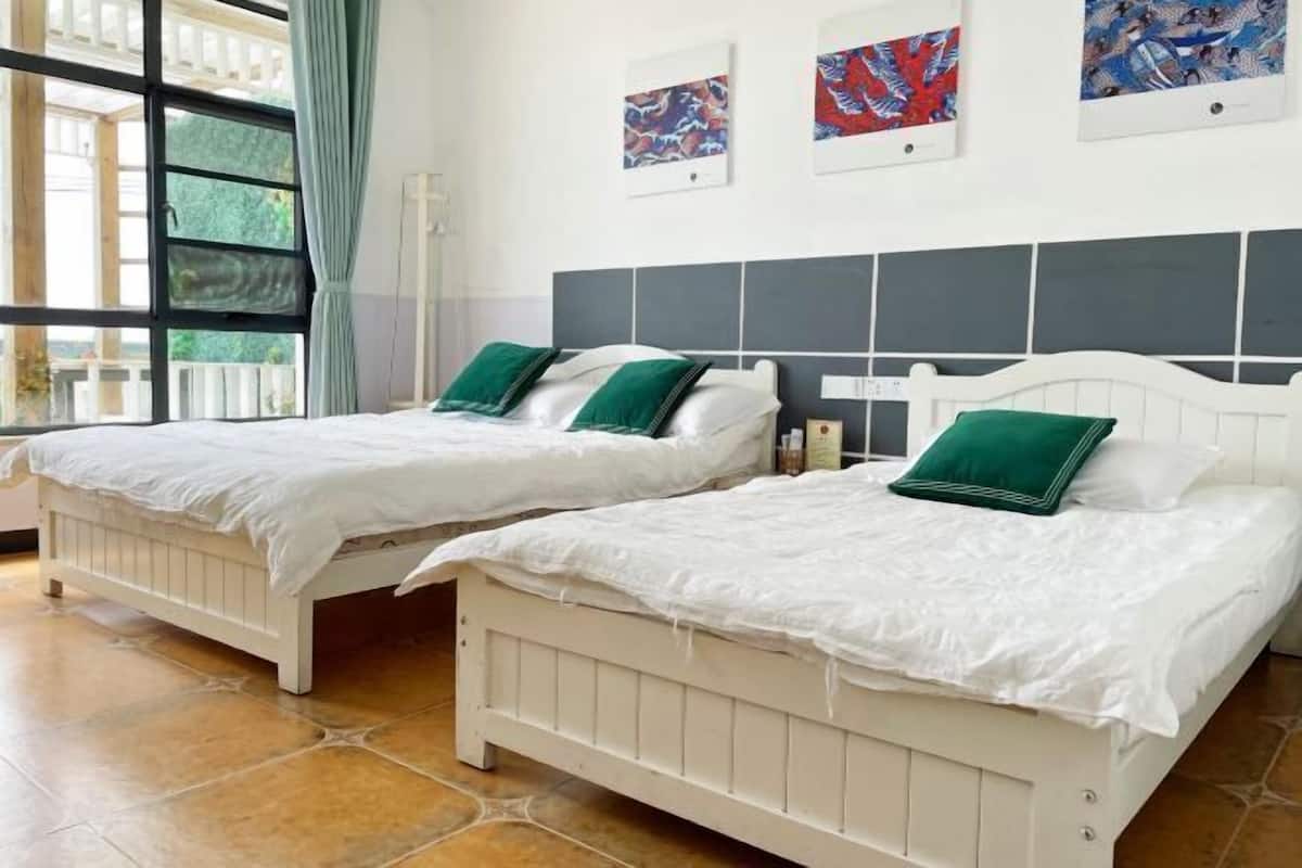 Una habitación con dos camas blancas, cada una con almohadillas verdes, un cabecero gris y una ventana con cortinas.