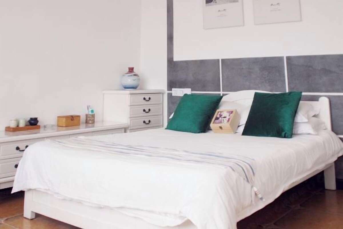 Une chambre à coucher avec un lit, des tables de chevet blanches, une commode et un mur orné de tableaux.
