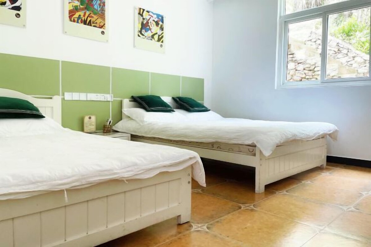 Une chambre avec deux lits, une fenêtre et des œuvres d’art accrochées au mur.