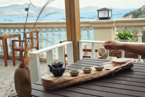 Une table en bois, sur laquelle sont disposés un service à thé et un vase, se trouve sur un balcon donnant sur la mer.