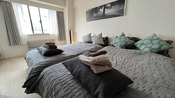 A bedroom with two beds, each with a duvet and pillows, a window with curtains, and a painting on the wall.