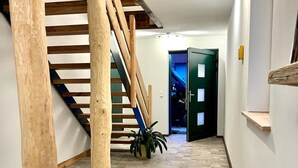 A hallway with a wooden staircase, a green door, and a potted plant.