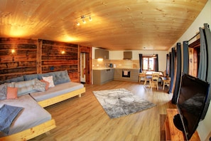 A cozy cabin interior with a wooden ceiling, a sofa, a dining table, and a television.