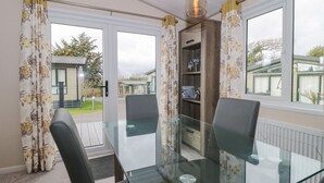 A dining area with a glass table and chairs, a wooden bookshelf, and a view of the outside. - Gwydn Lodge (Lymington)