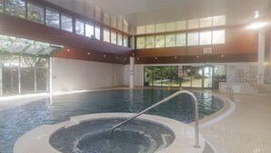 An indoor swimming pool with a hot tub, surrounded by large windows and a tiled floor. - Gwydn Lodge (Lymington)