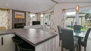 A modern kitchen with a central island, dining area with chairs, and a large window with curtains. - Gwydn Lodge (Lymington)
