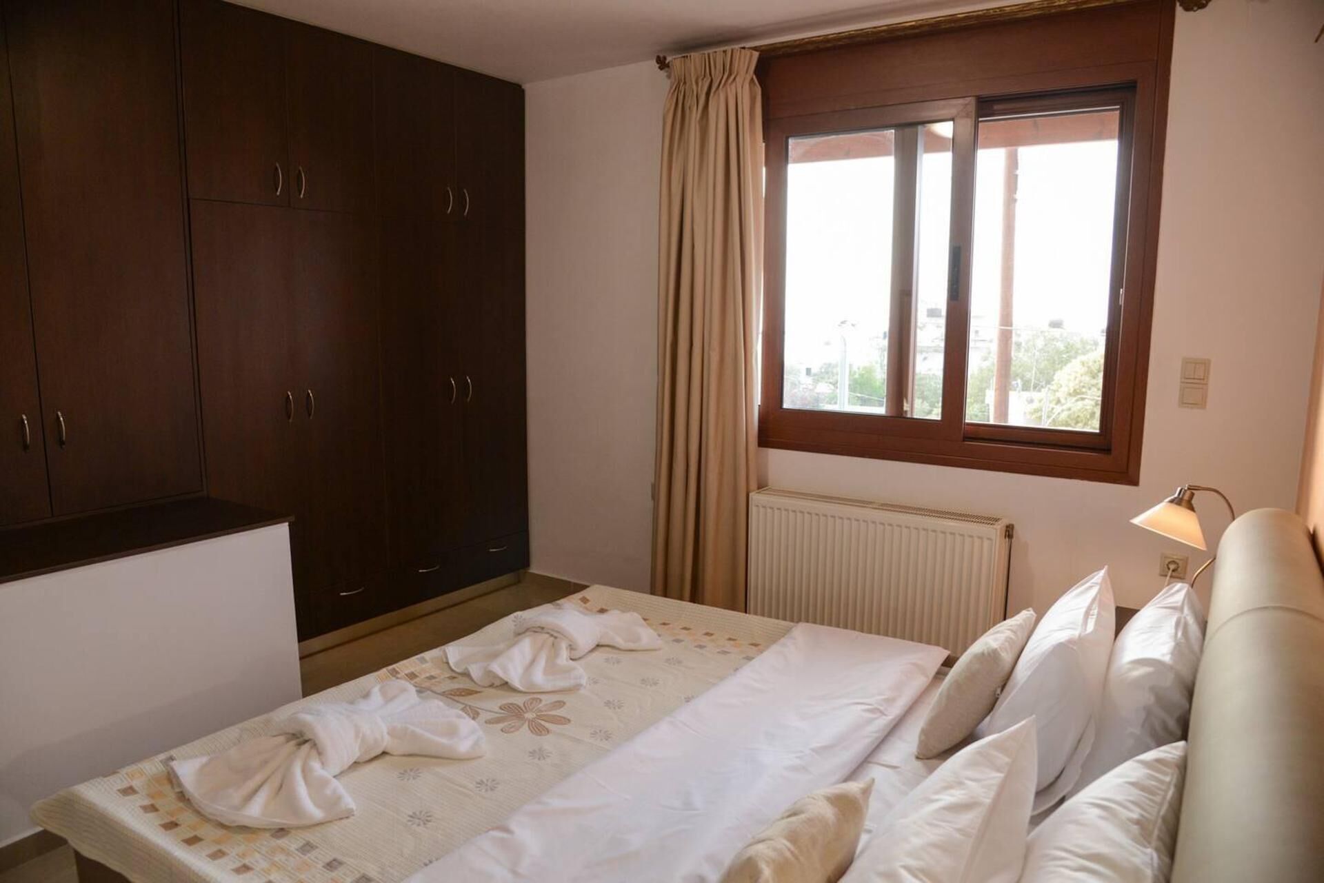 A bedroom with a bed, a wardrobe, a window with curtains, and a radiator.