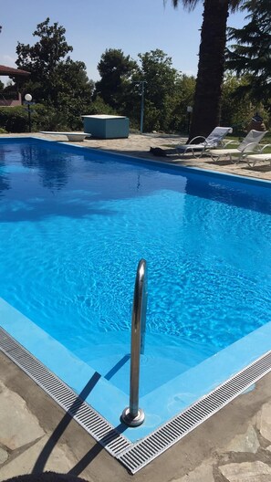 Une piscine dotée d’une rambarde métallique, entourée d’une terrasse en pierre et de chaises longues.