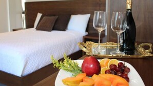 Un lit bien fait, avec du linge de lit blanc et des oreillers marron, une table de chevet sur laquelle se trouve un plateau avec une bouteille de champagne, deux verres et une assiette de fruits.