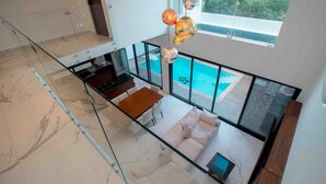 Un intérieur moderne avec une balustrade en verre, un coin repas, une cuisine et une vue sur une piscine.