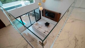 Un intérieur moderne avec une balustrade en verre, un canapé, une cheminée et une vue sur la verdure à l’extérieur.