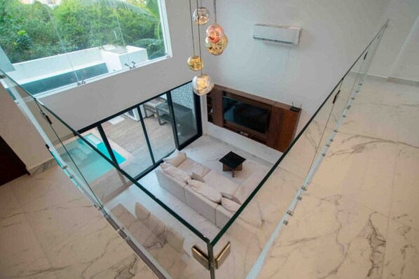 A modern interior with a glass railing, a sofa, a fireplace, and a view of greenery outside.