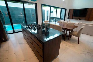 A modern kitchen with a central island, a dining area with a table and chairs, and a large TV mounted on the wall.