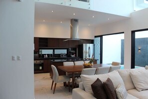 A modern kitchen with dark cabinetry, a central island, and a dining area with a white table and chairs.