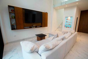 A modern living room with a large flat-screen TV, a white sofa, and a small table.