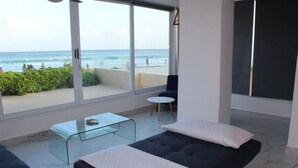 Ein modernes Schlafzimmer mit großem Fenster mit Blick auf einen Strand, einem Glastisch und einem gemütlichen Bett.