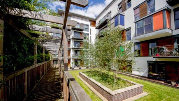A modern apartment complex with multiple balconies, a central courtyard with a tree, and a wooden staircase. - Amazing Riverside Boheme Home in SW London! (London)