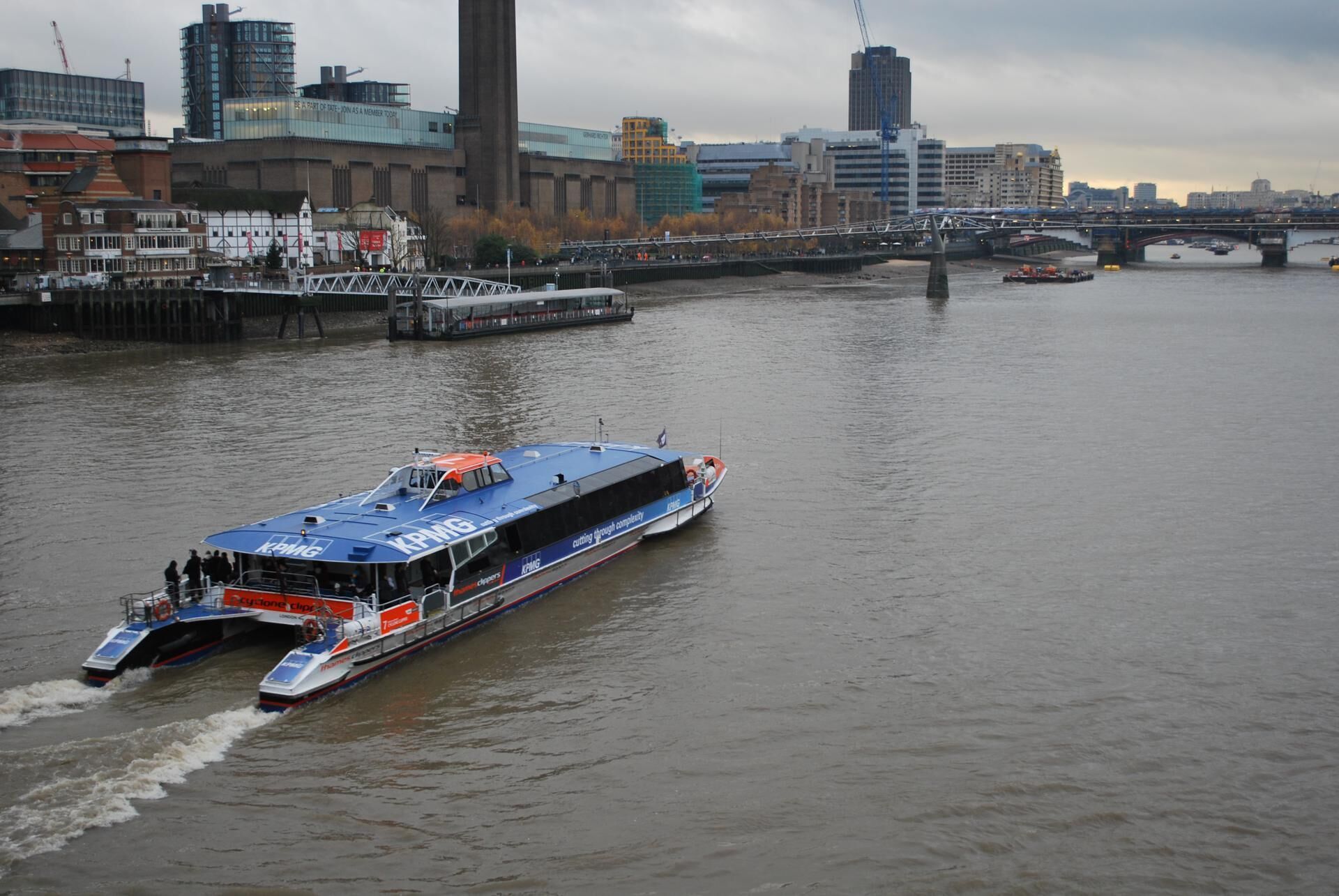 A riverboat with 'KPMG' branding on a river, surrounded by buildings and a bridge in the background.