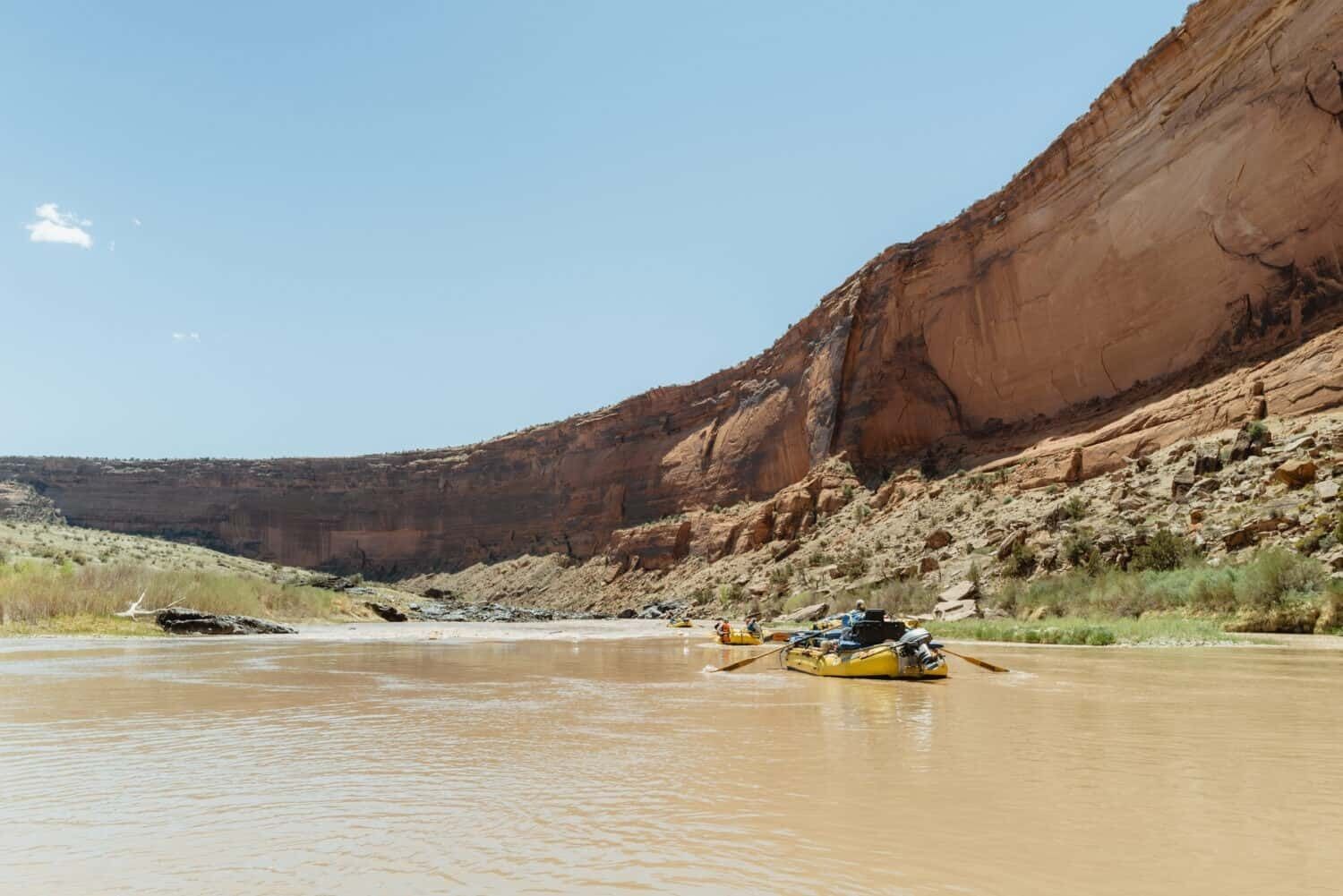 A river with a yellow raft and a rocky cliff in the background.