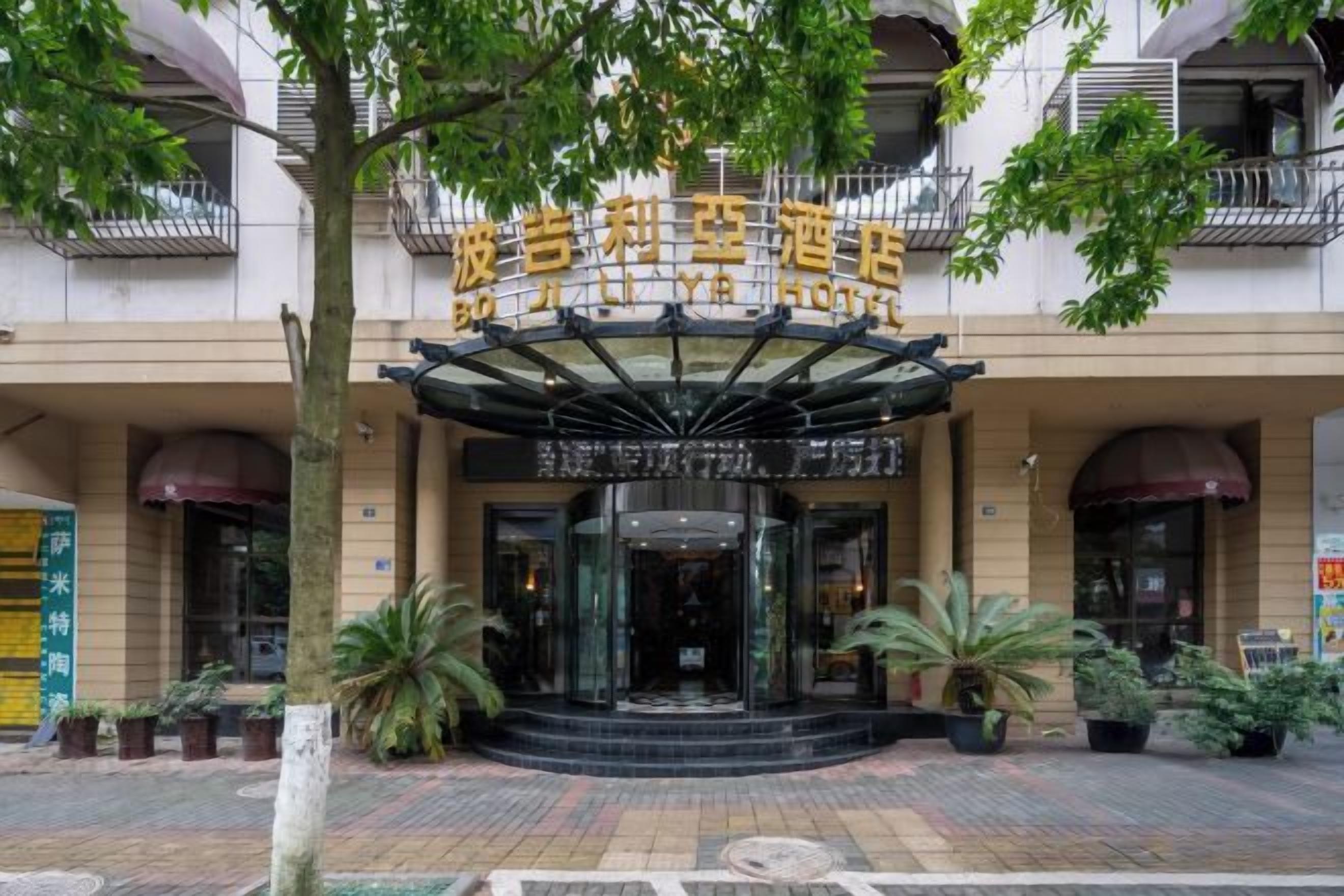 A hotel entrance with a glass facade, a canopy, and potted plants.