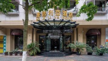 A hotel entrance with a glass facade, a canopy, and potted plants.
