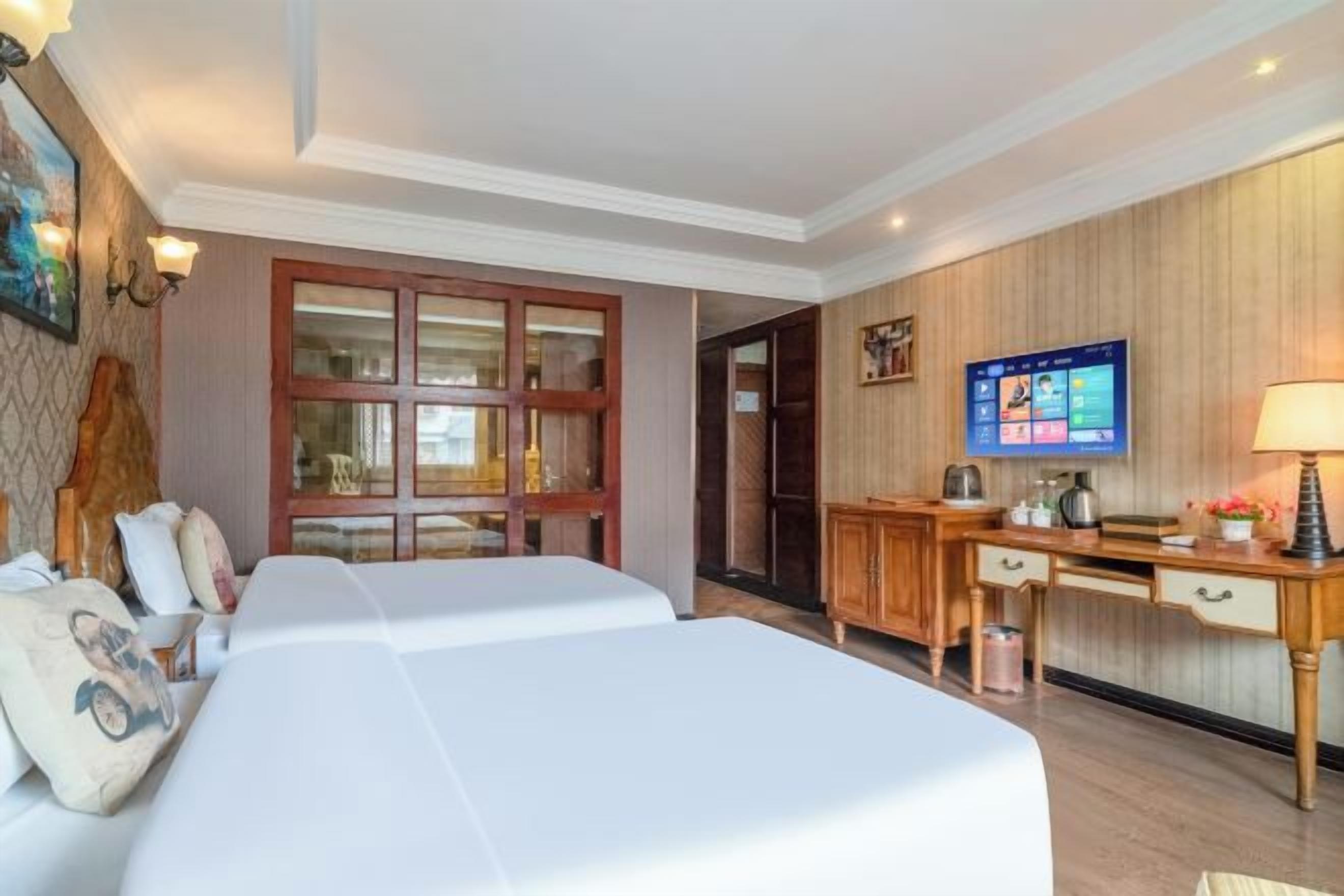 A hotel room with two beds, a desk with a computer, a television, and a wooden wall panel.