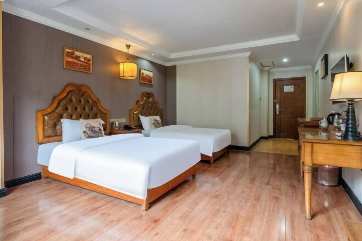 Een hotelkamer met twee bedden, houten vloeren, een bureau met een lamp en een deur.