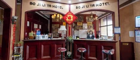 A reception area with a wooden counter, two bar stools, and a red decorative hanging.