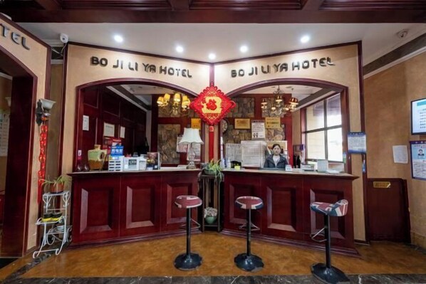Un espace d’accueil avec un comptoir en bois, deux tabourets de bar et une décoration murale rouge.