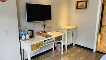 A small, clean room with a desk, a television, a cabinet, and a trash can.
