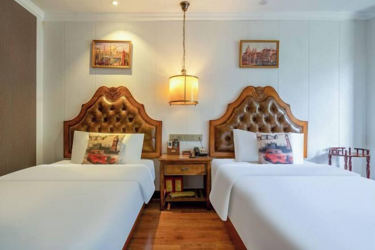 Een hotelkamer met twee bedden, houten hoofdeinden, een nachtkastje met een lamp en kunstwerken aan de muren.