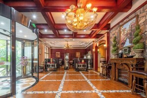 Un'elegante hall d'albergo con un lampadario imponente, una reception e un camino decorativo.